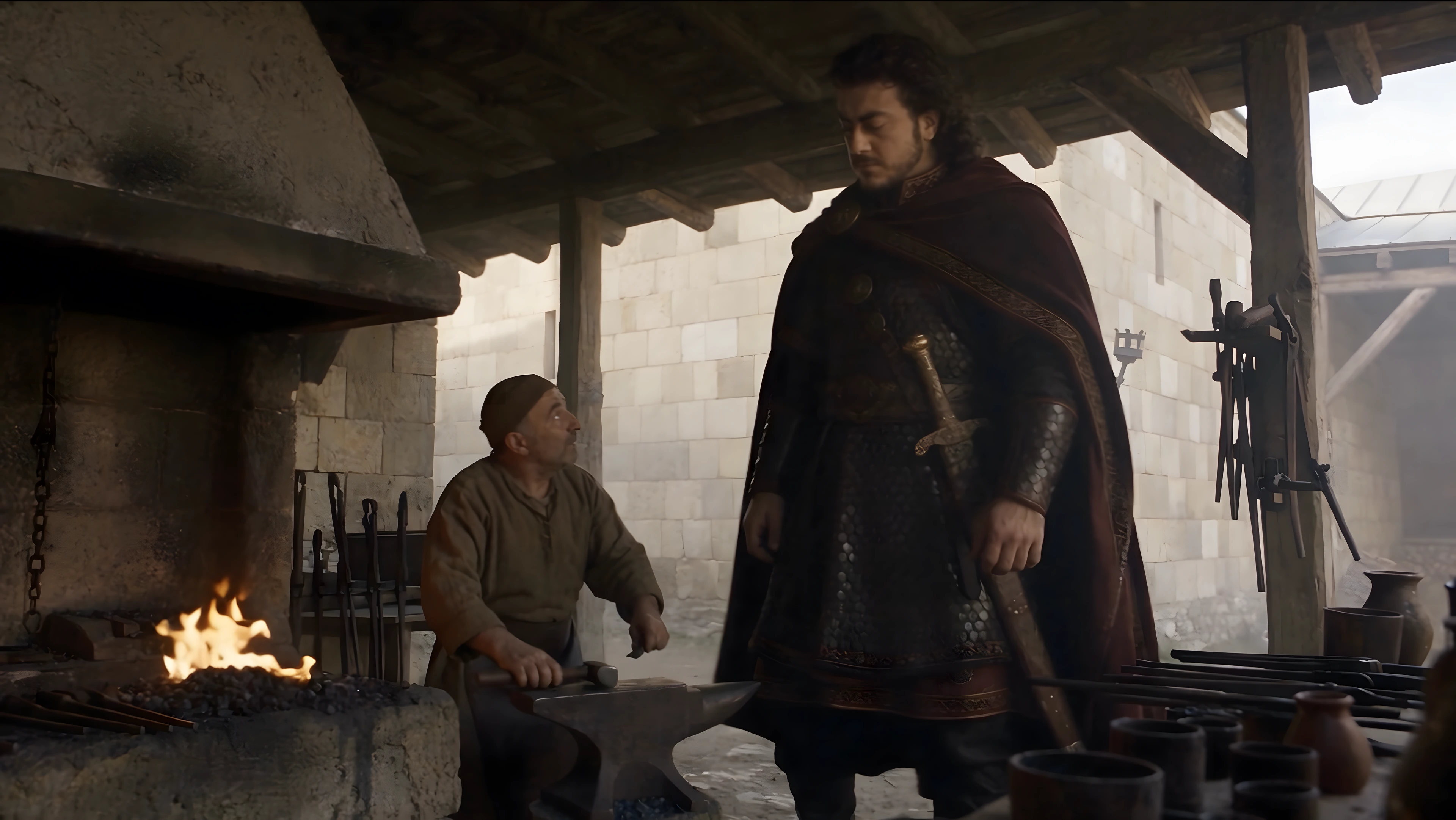 Vakhtang stands beside a seated smith and a glowing forge in a stone workshop.